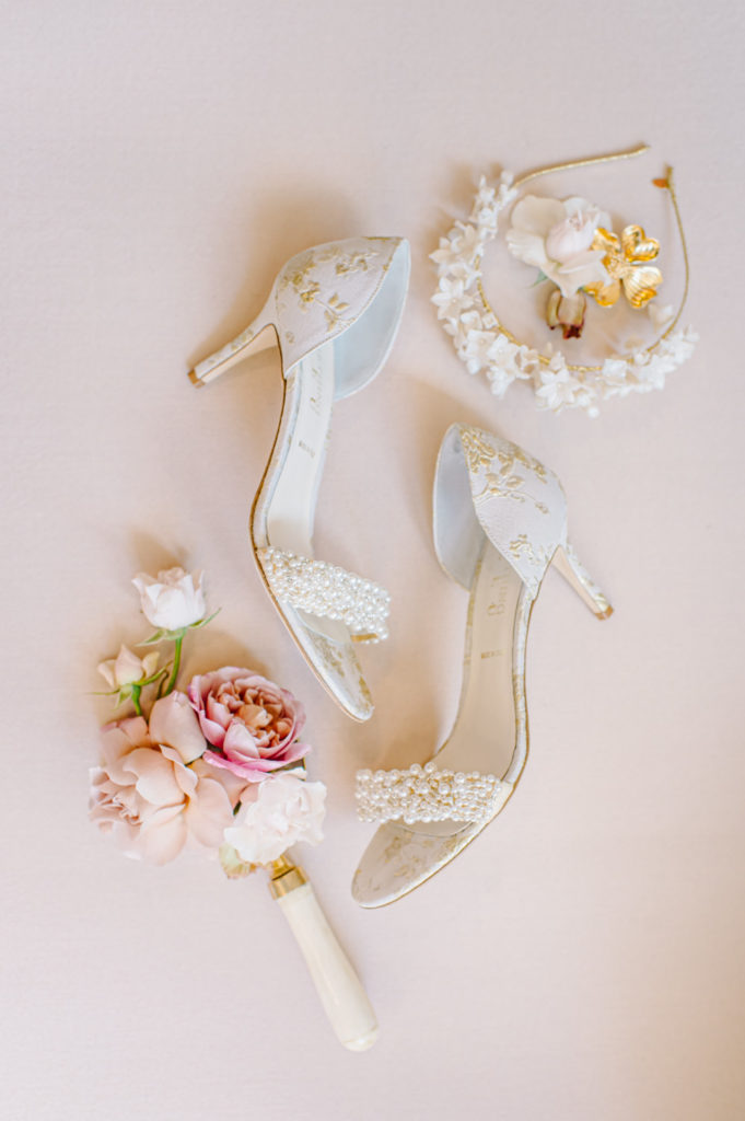 White bridal shoes with gold accents, complemented by roses and a floral headband, creating a beautiful ensemble for the bride. L Hewitt Photography

