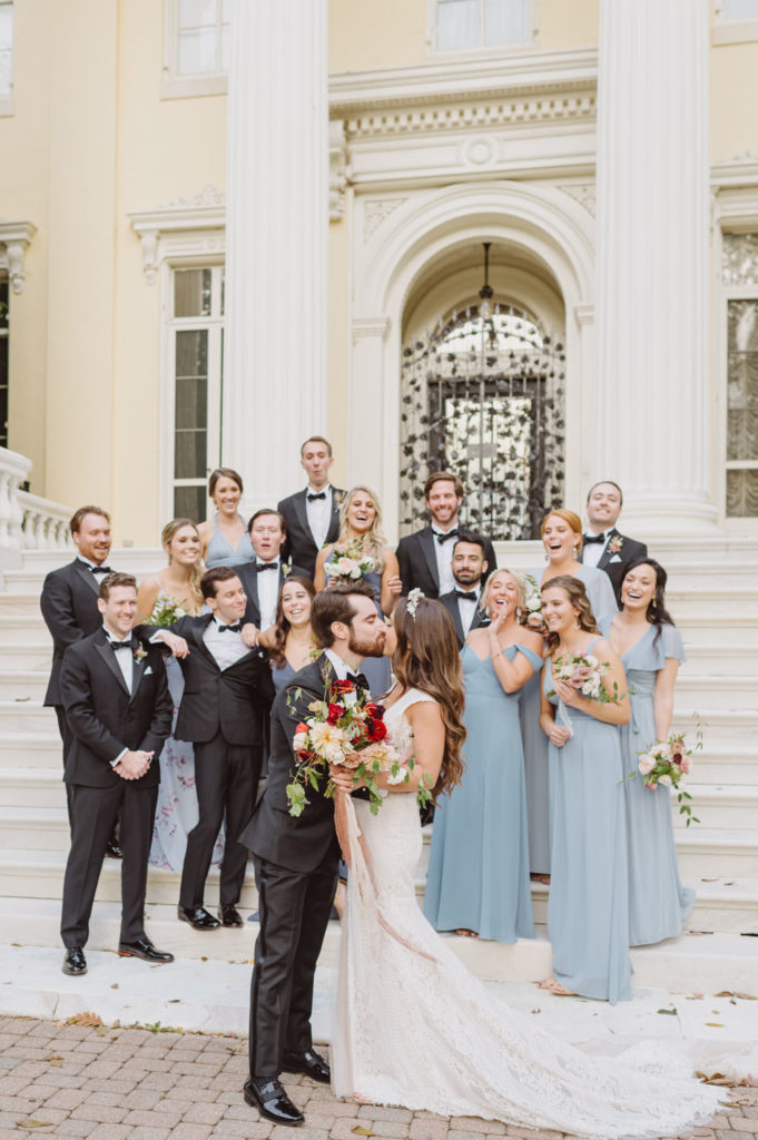The couple shares a heartfelt kiss amidst the presence of their joyous bridal party. L Hewitt Photography

