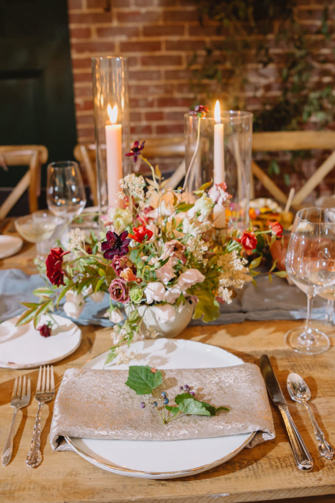 A beautiful floral centerpiece and light pink candles grace the tables, contributing to the enchanting feel of the wedding reception. L Hewitt Photography

