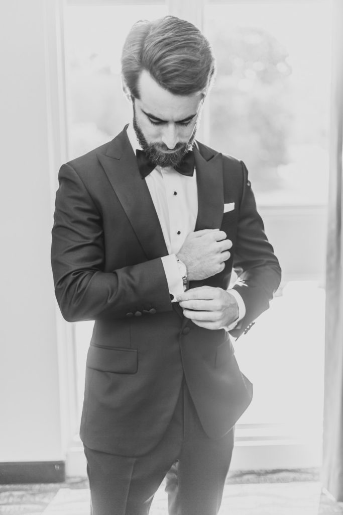 A captivating black and white photo of the groom getting ready and attentively fixing his sleeve in preparation for the ceremony. L Hewitt Photography

