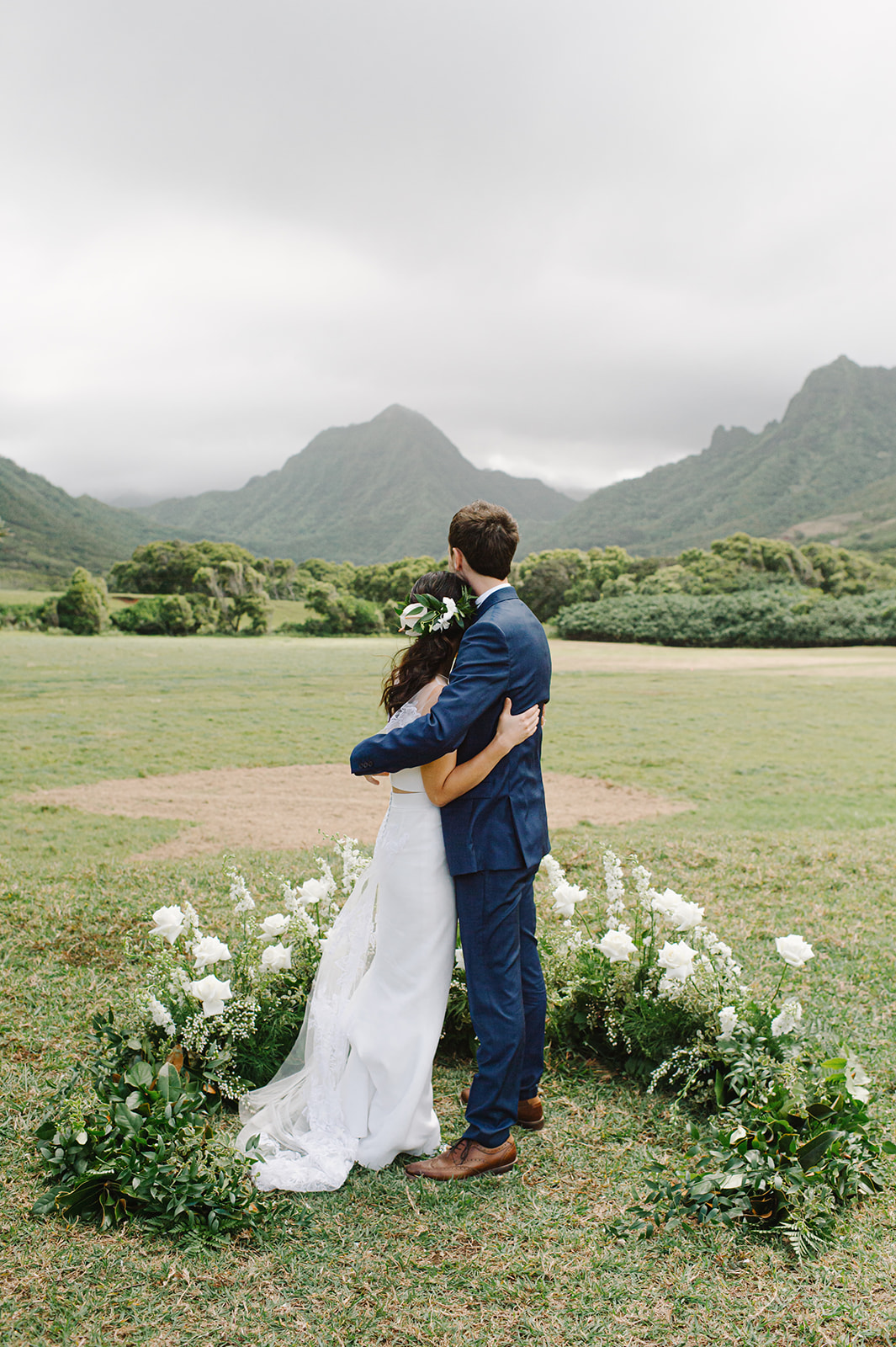 Enchanting embrace of the bride and groom amidst white florals, with the majestic mountains providing a breathtaking backdrop L Hewitt Photography