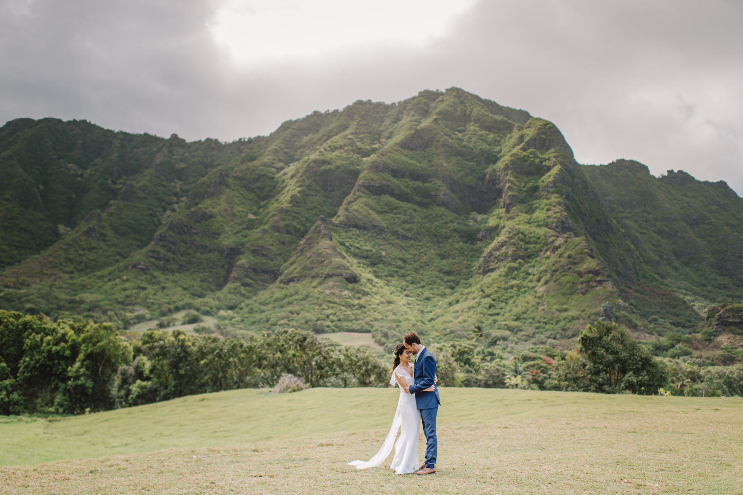 Romantic embrace after the ceremony, framed by the stunning beauty of the Oahu mountains L Hewitt Photography