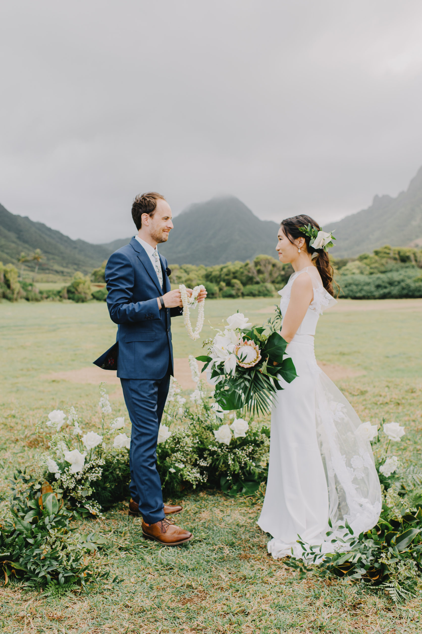  Intimate shot of the couple standing face to face, exchanging leis amidst the beauty of Low Camp at Kualoa Ranch L Hewitt Photography