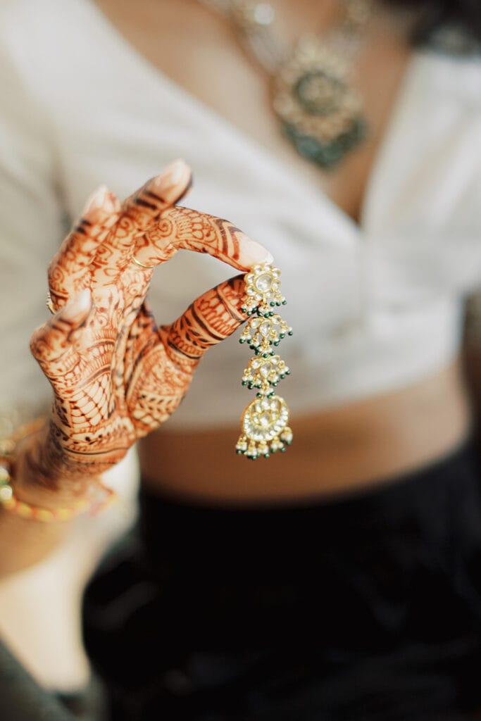 beautiful bride with wedding henna holding a beautiful Indian tassel earring for her Indian wedding ceremony at Capital One Hall. L Hewitt Photography
