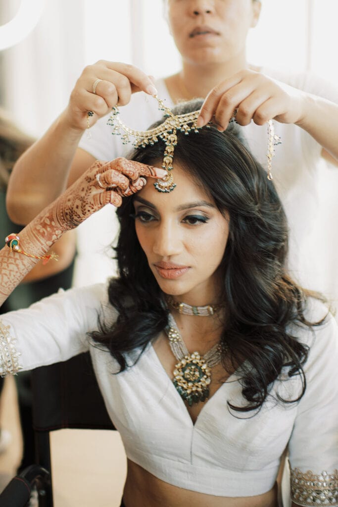 beautiful bride putting on a wedding tikka to prepare for her Indian wedding ceremony at Capital One Hall. L Hewitt Photography