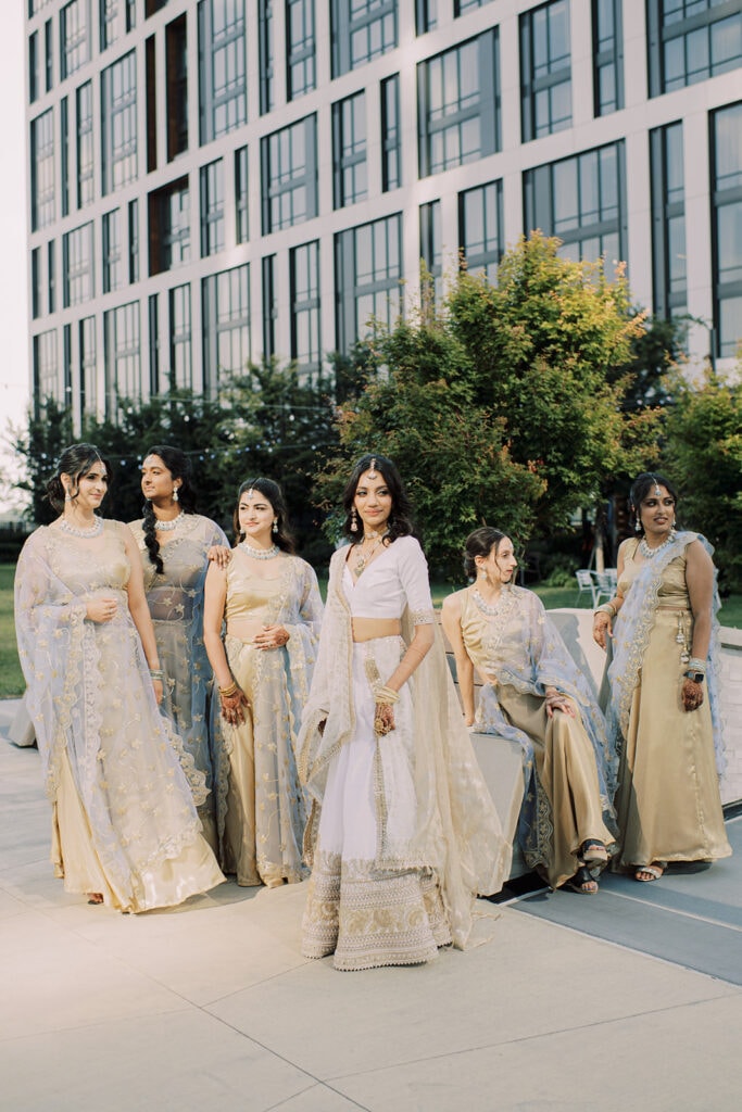 magazine moment of the beautiful bride wearing her white silver silk lehenga surrounded by her bridesmaids as they make their way to their Indian wedding reception at Capital One Hall. L Hewitt Photography