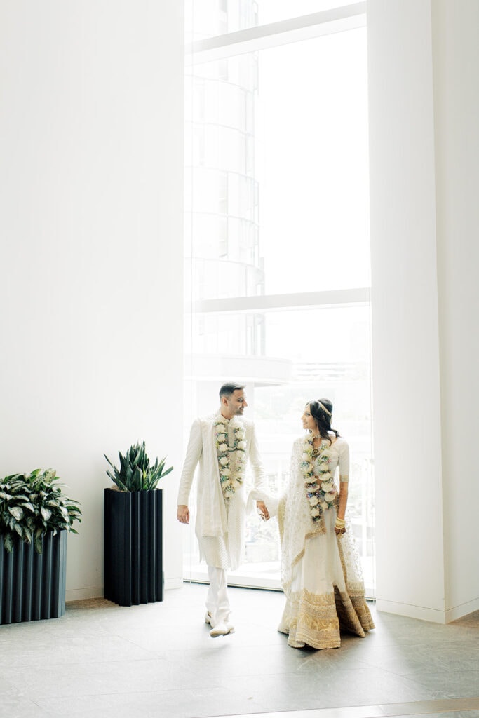 a romantic moment between beautiful bride wearing a white silk lehenga and a handsome groom wearing sherwani after their Indian wedding ceremony at Capital One Hall. L Hewitt Photography