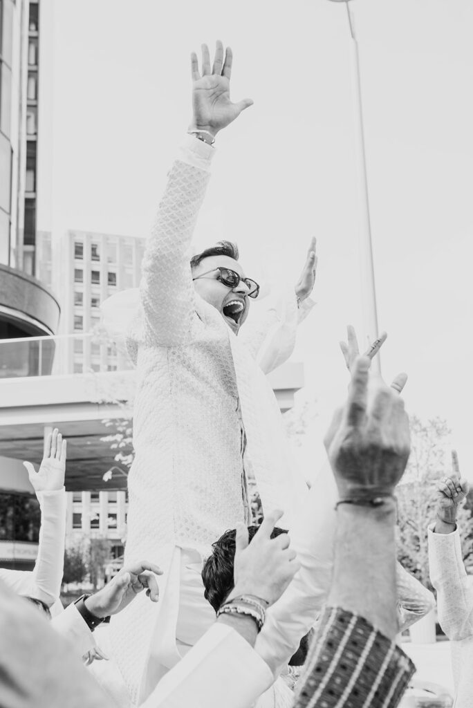 groom wearing sunglasses and white sherwani enjoying the baraat for his Indian wedding ceremony at Capital One Hall. L Hewitt Photography