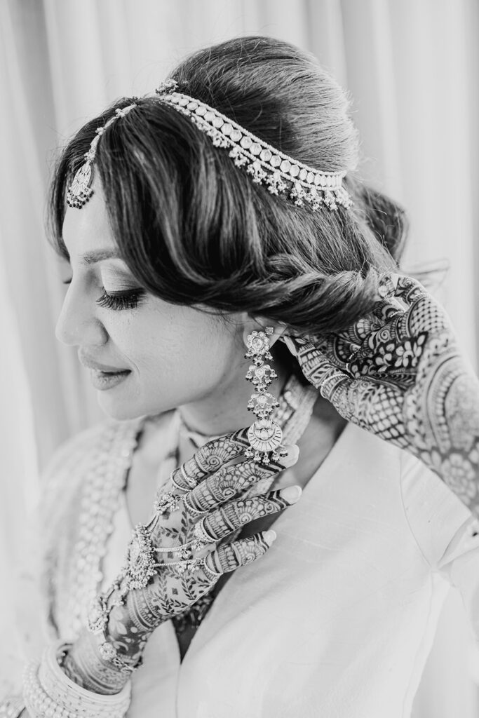 lovely bride with her wedding tikka, henna, and Indian tassel earrings as she dons on her silver white silk lehenga for her Indian wedding ceremony at Capital One Hall. L Hewitt Photography