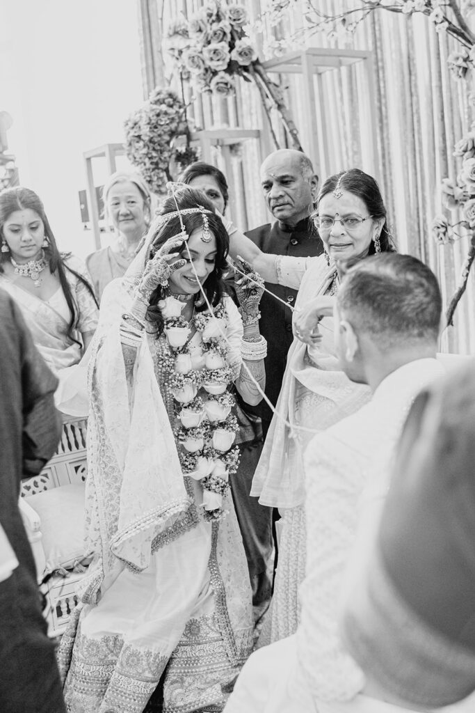 the garland exchange ceremony between the bride wearing a silver white silk lehenga and the groom wearing a white sherwani as they exchange white rose and baby’s breath garlands for their Indian wedding ceremony at Capital One Hall. L Hewitt Photography