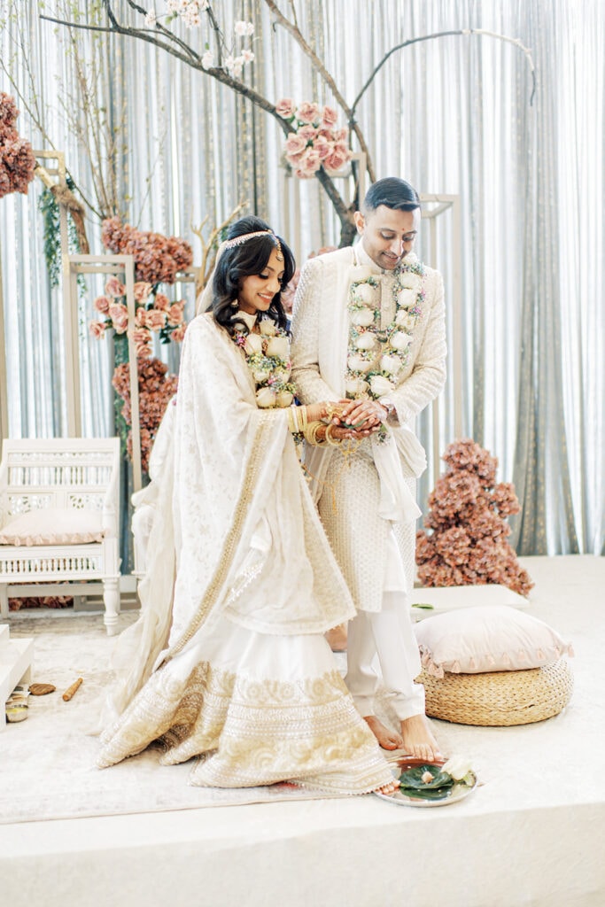 the bride wearing a gold white silk lehenga and the groom wearing a white sherwani  after the garland exchange ceremony for their Indian wedding ceremony at Capital One Hall. L Hewitt Photography