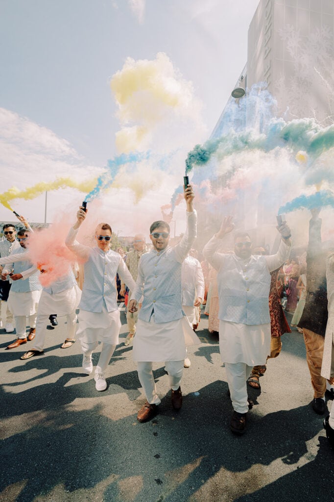 the groomsmen releasing pastel smoke bombs during baraat as the groom greets the bride of the family for their Capitol One Hall Indian Wedding. L Hewitt Photography